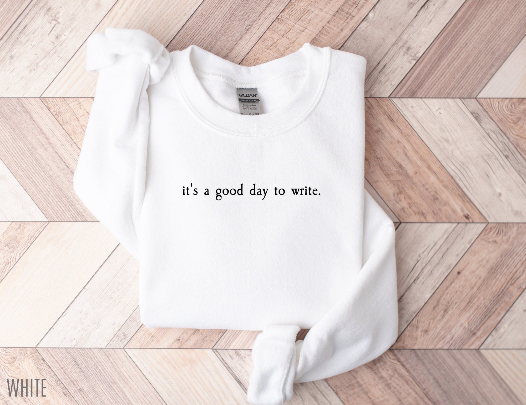 folded white sweatshirt with black minimalist text that says it's a good day to write