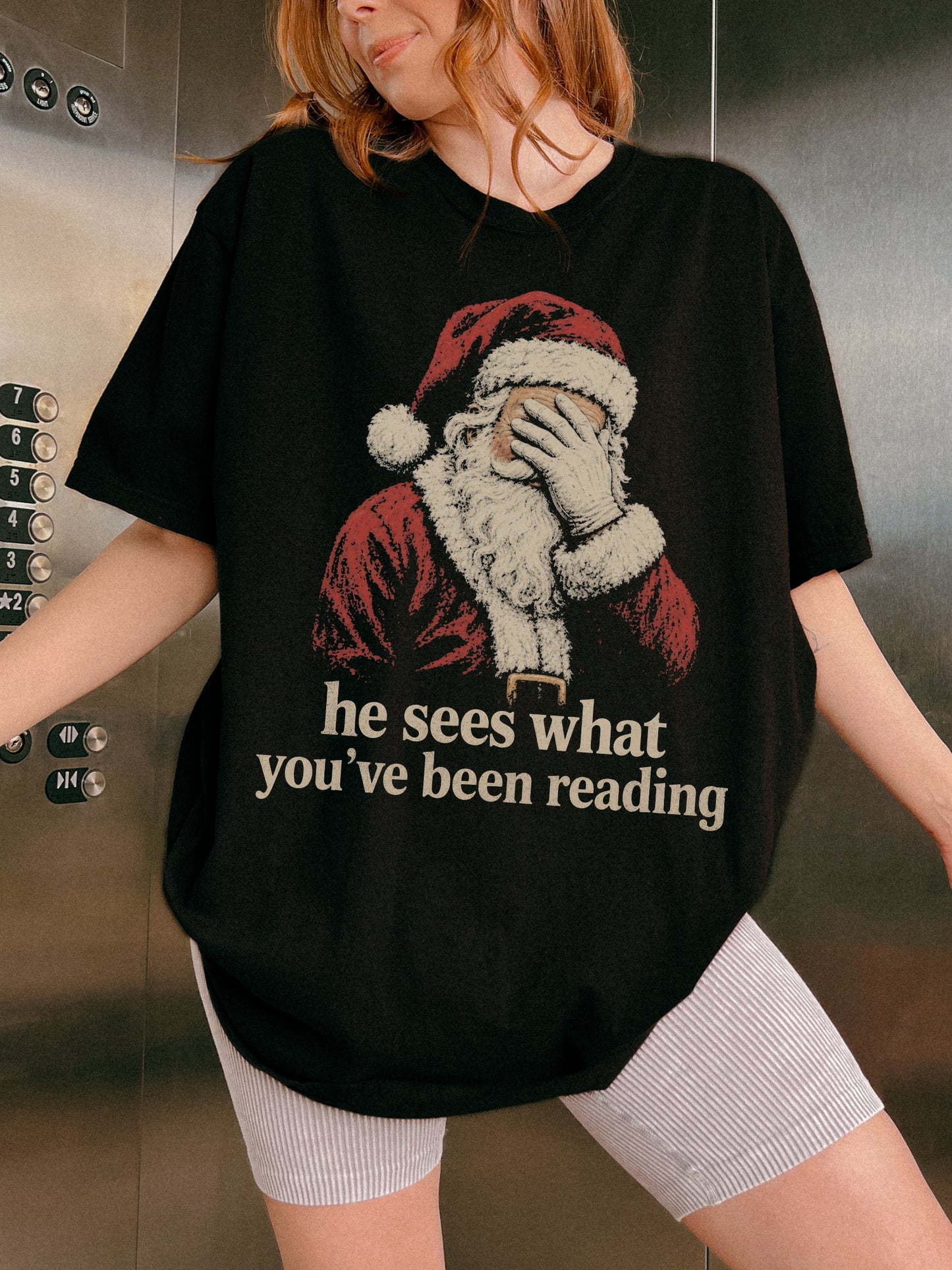 Black Comfort Colors shirt featuring vintage Santa covering his eyes with he sees what you’ve been reading text, a funny bookish Christmas shirt for readers and book lovers
