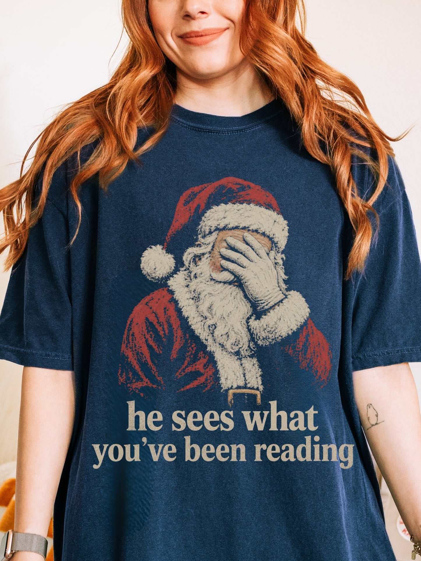 True Navy Comfort Colors shirt featuring vintage Santa covering his eyes and he sees what you’ve been reading text, a funny Christmas shirt for book lovers and readers
