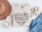 folded sand-colored sweatshirt with hand-drawn book stacks in a heart shape, styled with hat and jeans