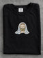 Black Comfort Colors shirt featuring a cute hedgehog reading a book while wrapped in a blue striped blanket, cozy bookish shirt for readers, book lovers and bookworms