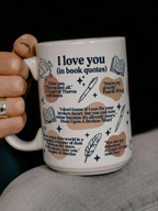 White ceramic I Love You in Book Quotes mug held in hand featuring romantic fantasy book quotes with dragon, book, feather, and star illustrations on cozy dark background