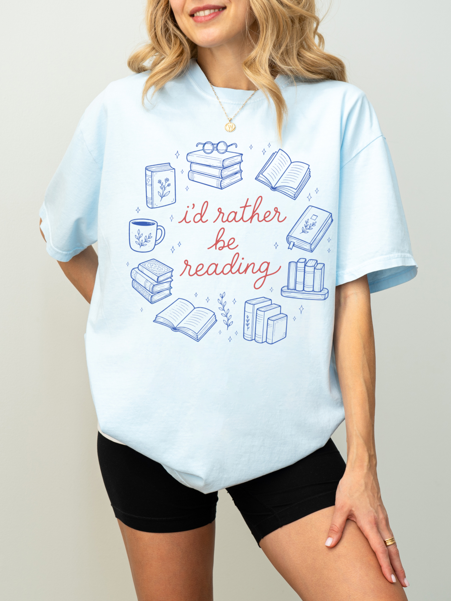 woman wearing light blue oversized reader t shirt with id rather be reading graphic featuring stacks of books open books and coffee cup illustrations
