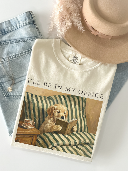 ivory comfort colors shirt flatlay with vintage painting of a dog reading a book on a striped couch with coffee cup aesthetic cozy outfit with denim jeans and beige hat