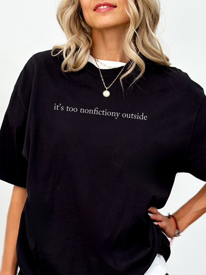 Woman wearing black Comfort Colors book lover shirt featuring minimalist text it's too nonfictiony outside styled with layered gold necklace