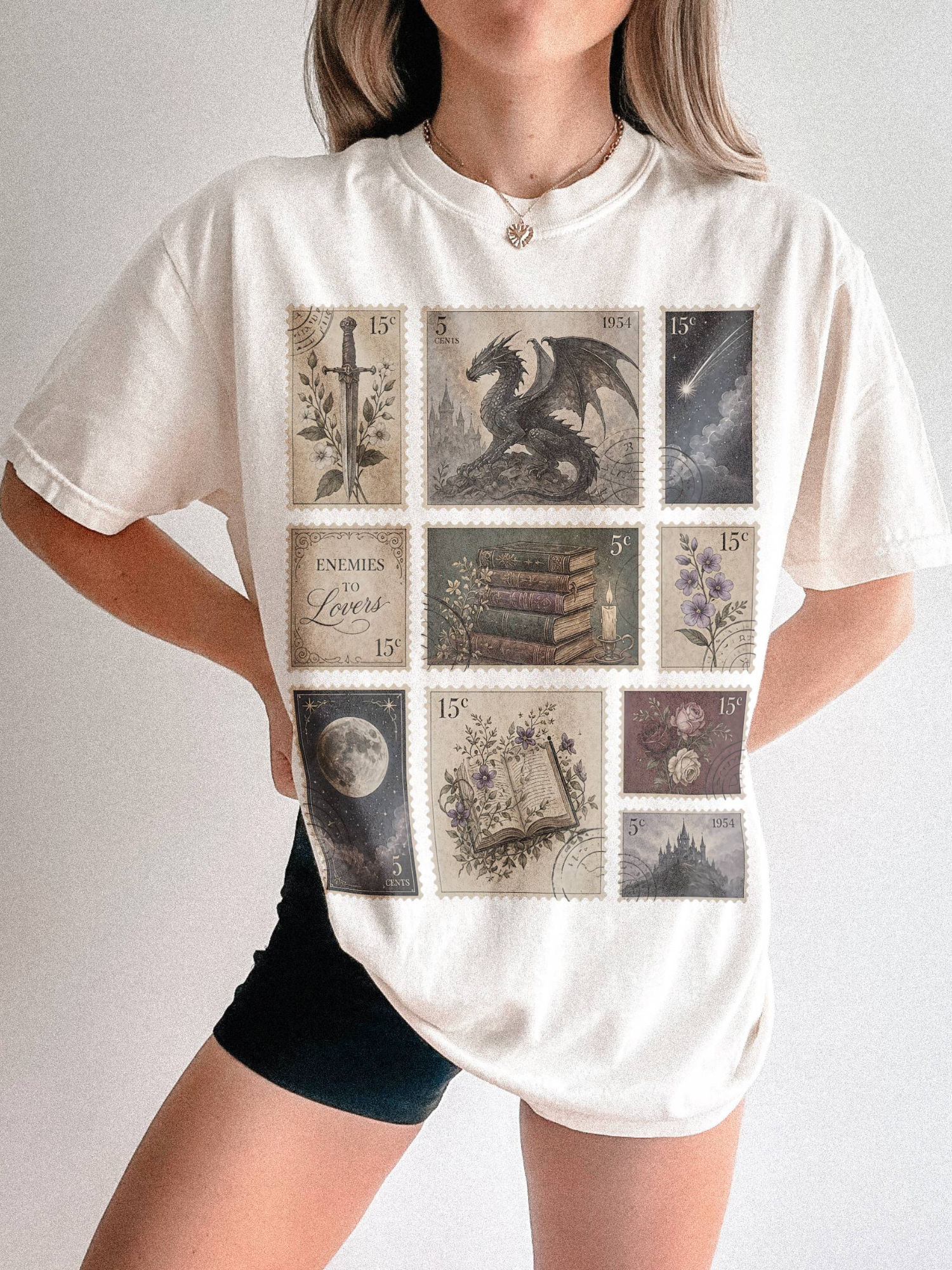 Woman wearing ivory oversized fantasy reader t shirt with vintage postage stamp collage featuring dragon moon antique books floral art castle and enemies to lovers design