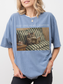 Woman wearing a blue jean t shirt with just one more chapter text and vintage style illustration of a cat reading a book on a striped couch with a teacup beside it