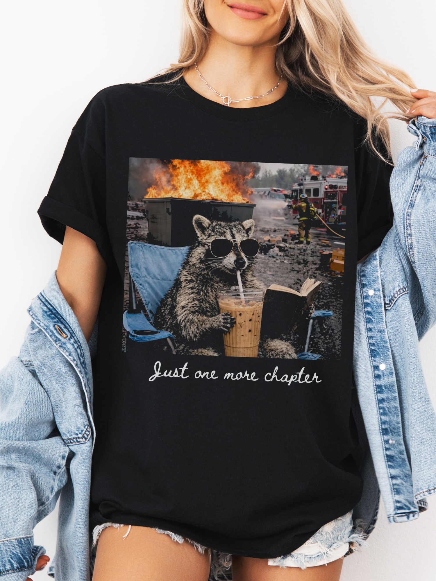black comfort colors oversized book lover shirt featuring raccoon drinking iced coffee reading during chaos graphic
