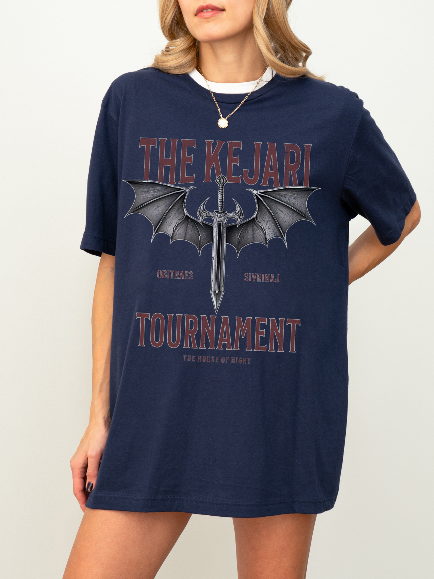 Front-facing shot of a woman wearing a navy blue Kejari Tournament fantasy book shirt with bold serif text, sword illustration with bat wings, and House of Night references for romantasy readers.