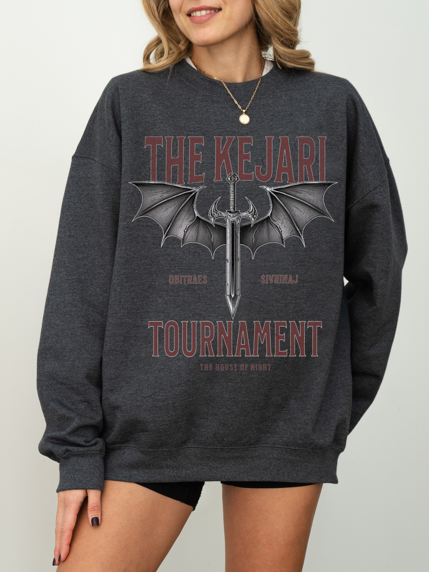 Dark heather grey fantasy bookish sweatshirt with Kejari Tournament design, woman poses with hand on hip and neutral smile