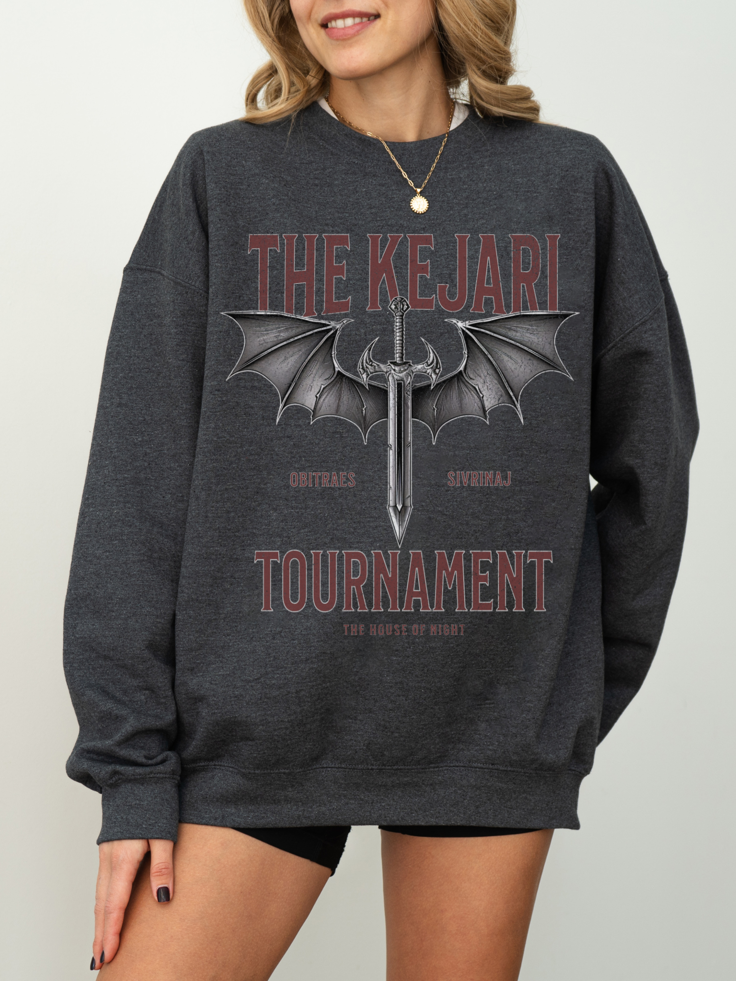 Dark heather grey fantasy bookish sweatshirt with Kejari Tournament design, woman poses with hand on hip and neutral smile