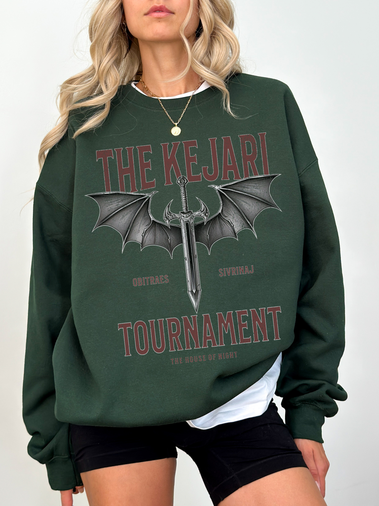 Forest green bookish sweatshirt styled with The Kejari Tournament design, model standing with hands at sides and white layering underneath