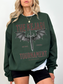 Forest green bookish sweatshirt styled with The Kejari Tournament design, model standing with hands at sides and white layering underneath