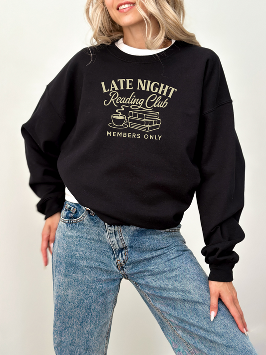 woman wearing a black sweatshirt that says late night reading club members only with light tan book and mug design
