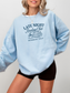 woman wearing a light blue sweatshirt that says late night reading club members only with navy mug and books graphic