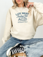 woman sitting cross-legged in a sand sweatshirt with late night reading club members only and navy blue graphic
