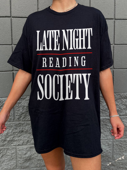 person wearing a black oversized t-shirt that says late night reading society in white text with red lines