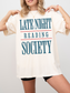 woman wearing a natural t-shirt that says late night reading society in teal blue text with red accent lines