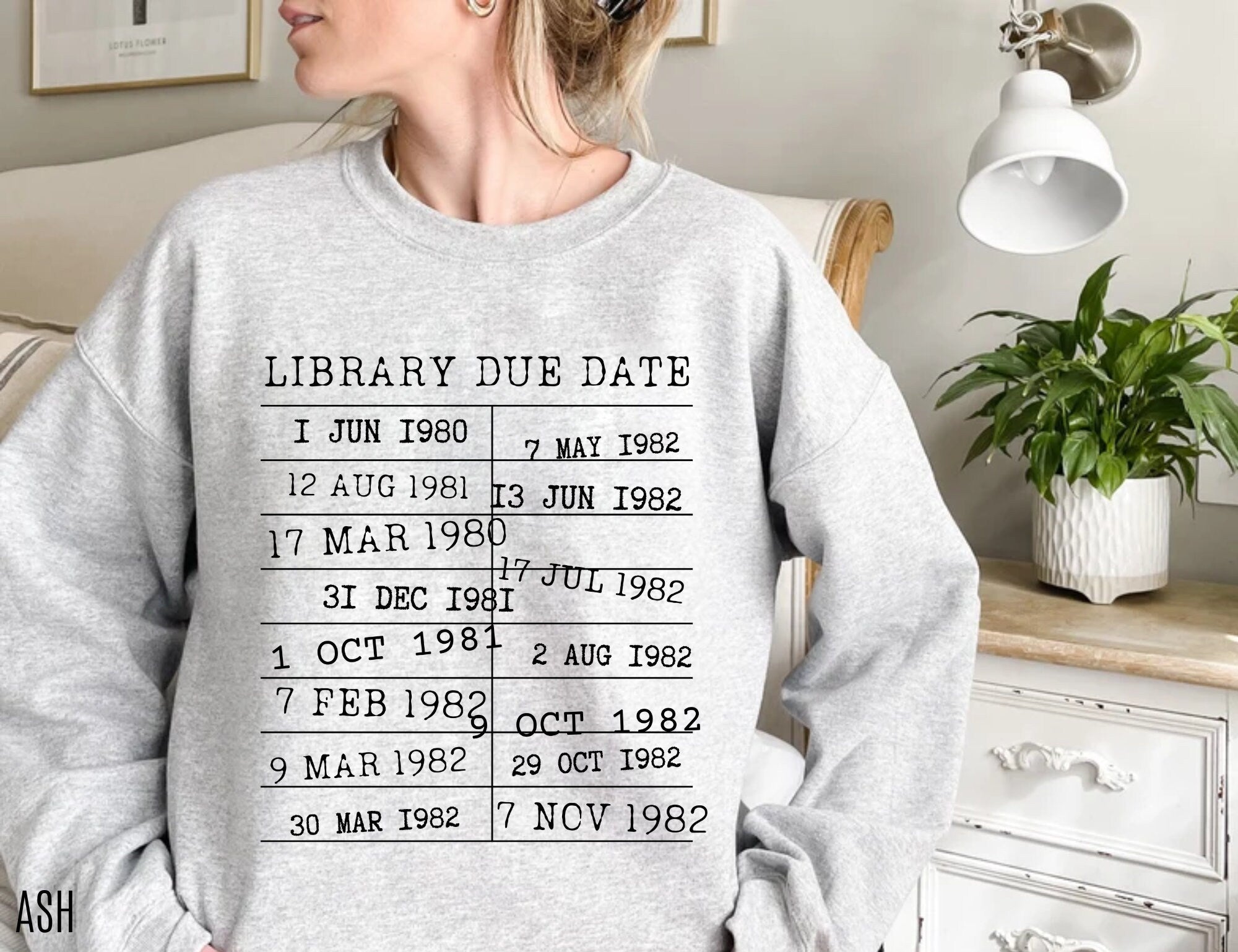 woman wearing ash grey sweatshirt with retro black text of library due date stamps