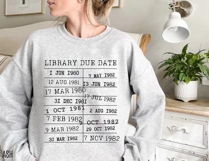 woman wearing ash grey sweatshirt with retro black text of library due date stamps