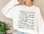woman in oversized white library due date sweatshirt with black stamped text, sitting indoors