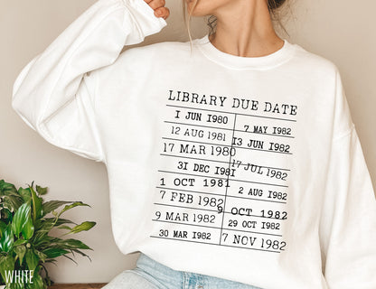 woman in oversized white library due date sweatshirt with black stamped text, sitting indoors