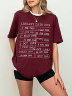 woman in a maroon t-shirt with white retro library date stamp graphic, paired with black shorts
