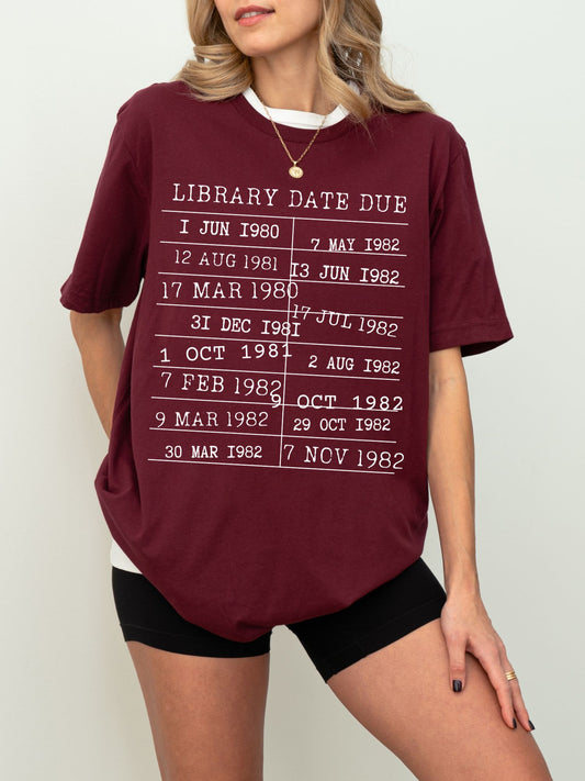 woman in a maroon t-shirt with white retro library date stamp graphic, paired with black shorts