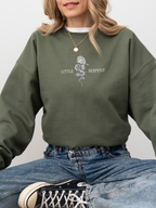 Army green bookish sweatshirt worn by smiling woman, showing Little Serpent graphic with rose and snake, cozy fantasy book apparel