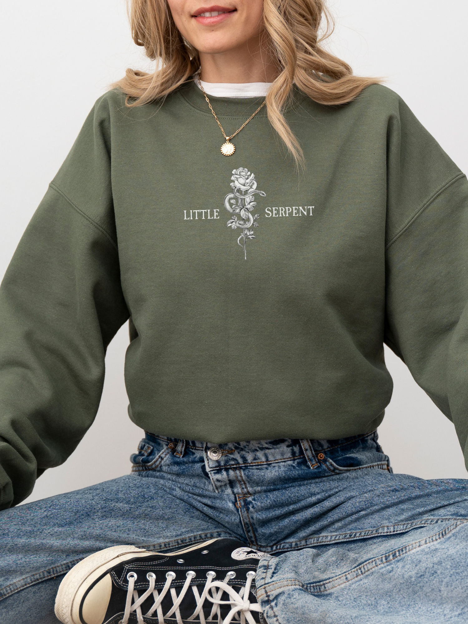 Army green bookish sweatshirt worn by smiling woman, showing Little Serpent graphic with rose and snake, cozy fantasy book apparel