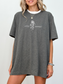 Model wearing a dark heather grey t-shirt with a minimalist fantasy design showing a snake and rose illustration between the words Little Serpent, officially licensed The Serpent and the Wings of Night apparel.
