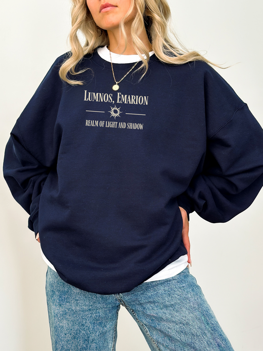 Woman wearing a navy Gildan sweatshirt with fantasy quote “Lumnos, Emarion,” styled with a layered white shirt and blue jeans.