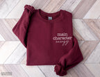 folded maroon sweatshirt with main character energy text on wood herringbone background