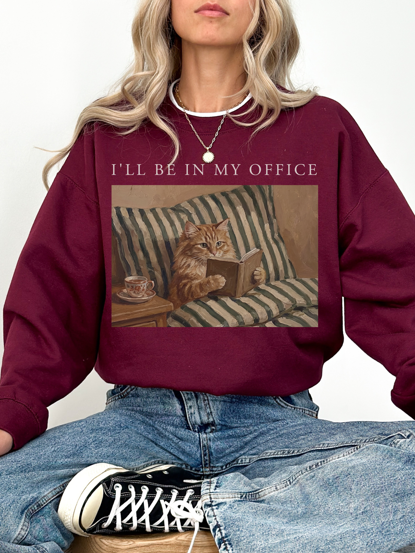 Maroon oversized sweatshirt featuring Ill be in my office text and a vintage cat reading a book design with striped bedding and tea cup detail. Warm cozy outfit for book lovers, readers, and cat themed fashion.
