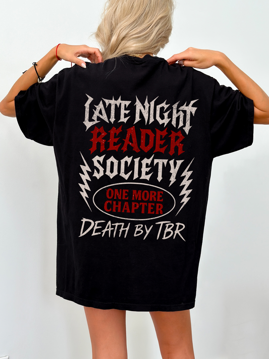 Oversized black t-shirt worn by a blonde woman, showcasing a bold metal-inspired back design with the text “Late Night Reader Society,” “One More Chapter,” and “Death by TBR” in grungy gothic fonts. Ideal gift for fantasy bookworms who stay up reading.