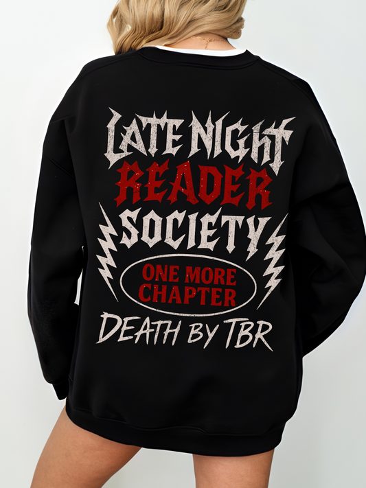A black sweatshirt with a bold heavy metal-inspired graphic that says Late Night Reader Society in distressed white and red letters, surrounded by lightning bolts. Centered below is a red oval with the words One More Chapter and underneath it reads Death by TBR. The sweatshirt is worn oversized on a blonde model standing with her back to the camera.