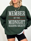 woman wearing a forest green sweatshirt with member of the midnight reading society in large white and red print