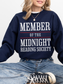 woman sitting in a navy sweatshirt with large white and red text that says member of the midnight reading society