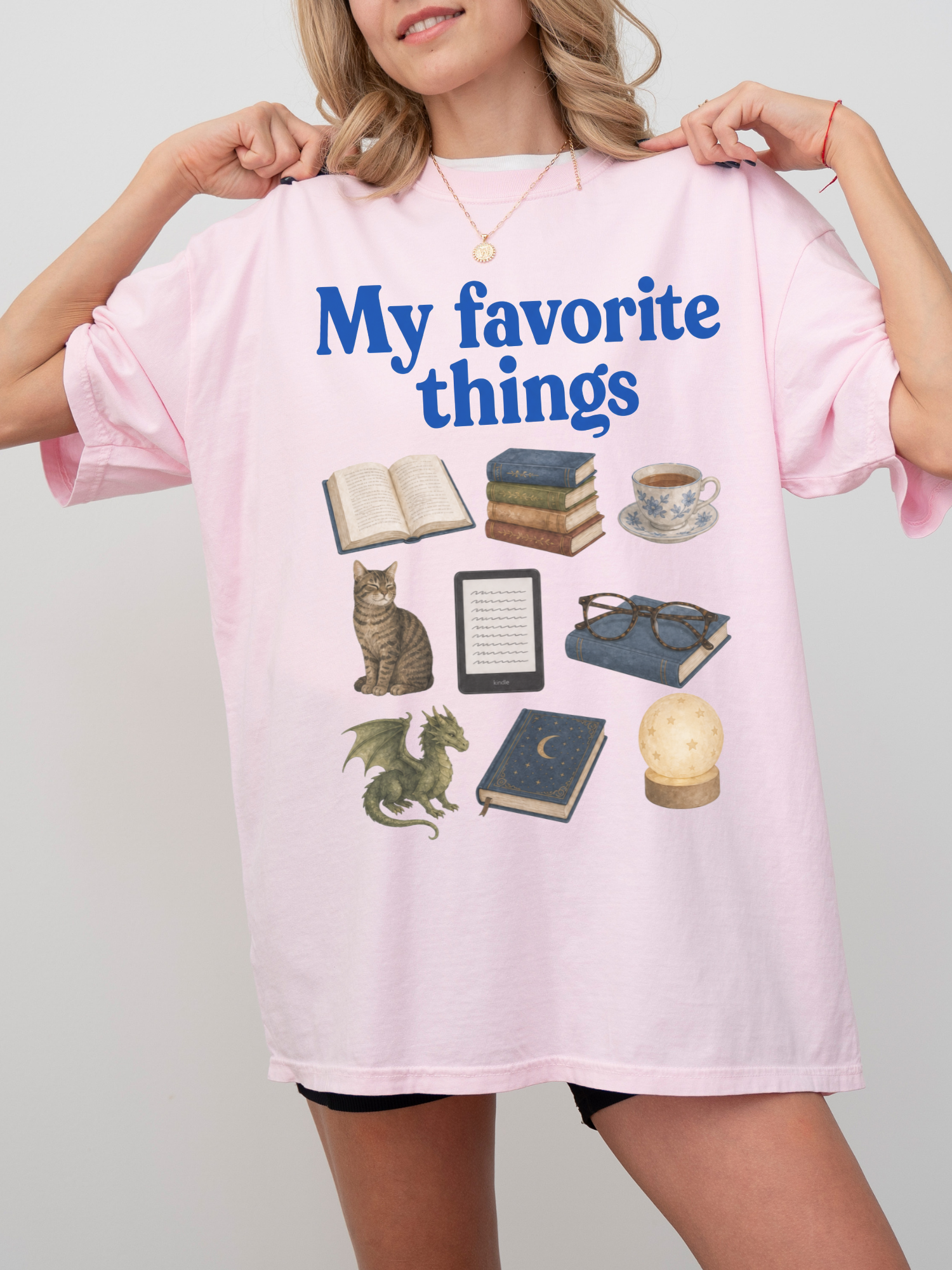 Woman wearing a blossom Comfort Colors shirt featuring My Favorite Things design with books, coffee, cat, Kindle, dragon, glasses, moon journal, and cozy reading essentials