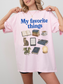 Woman wearing a blossom Comfort Colors shirt featuring My Favorite Things design with books, coffee, cat, Kindle, dragon, glasses, moon journal, and cozy reading essentials