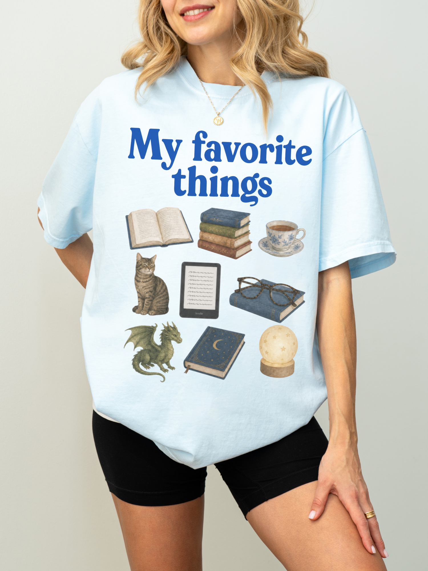 Woman wearing a chambray Comfort Colors shirt featuring My Favorite Things design with books, coffee, cat, Kindle, dragon, glasses, moon journal, and cozy reading essentials