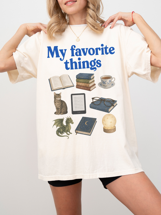 Woman wearing an ivory Comfort Colors shirt featuring My Favorite Things design with books, coffee, cat, Kindle, dragon, glasses, moon journal, and cozy reading essentials for book lovers