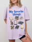Woman wearing an orchid Comfort Colors shirt featuring My Favorite Things design with books, coffee, cat, Kindle, dragon, glasses, moon journal, and cozy reading essentials