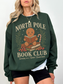 Close-up of forest green North Pole Book Club sweatshirt with gingerbread man sitting on books, candy cane, and festive winter greenery