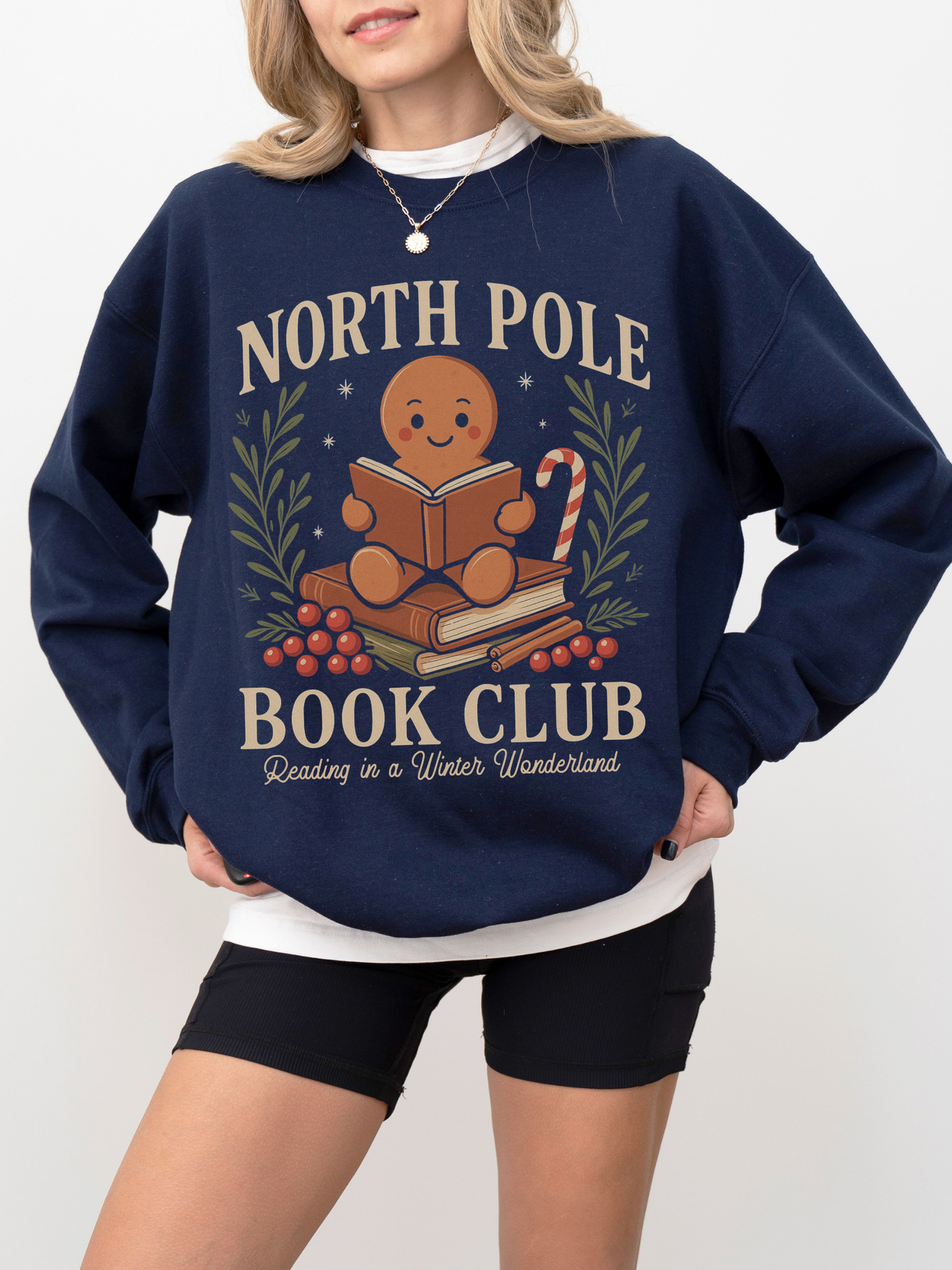 Model wearing navy blue North Pole Book Club sweatshirt with gingerbread design, books, and Christmas accents