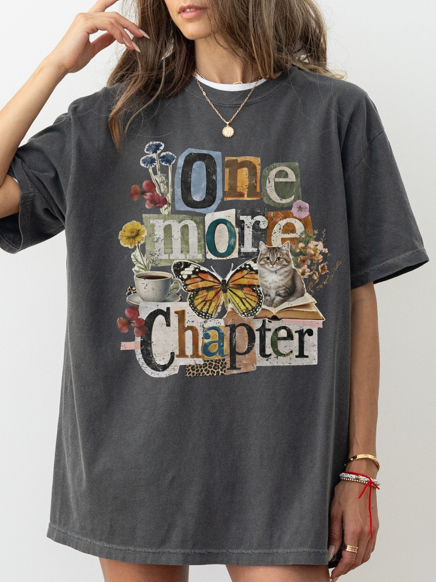 A woman wearing an oversized pepper graphic T-shirt with the phrase 'One more Chapter' in mixed typography, decorated with flowers, a butterfly, a cat, and books.