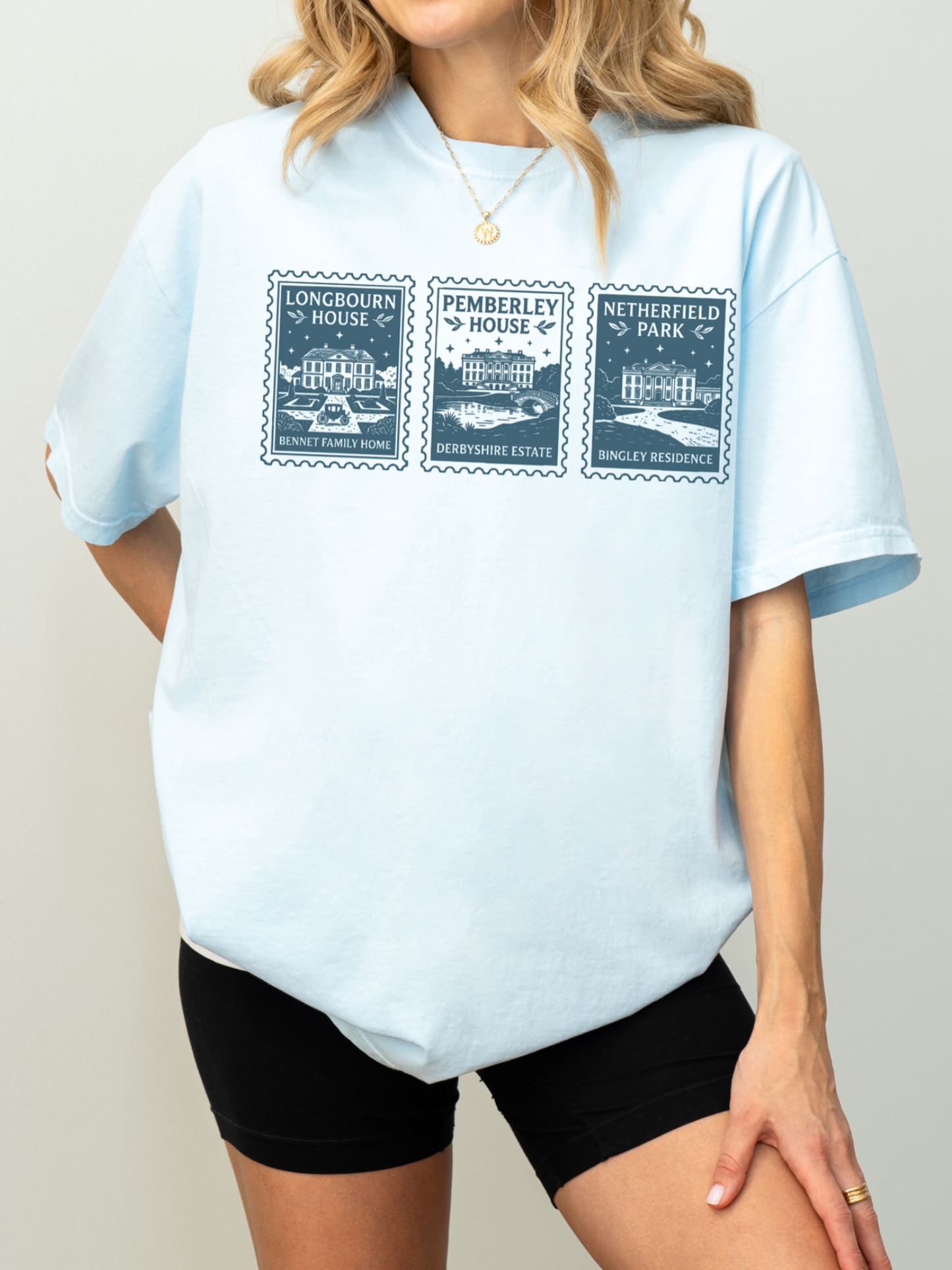woman wearing light blue t shirt with vintage stamp illustrations of Longbourn House Pemberley House and Netherfield Park classic literature inspired apparel