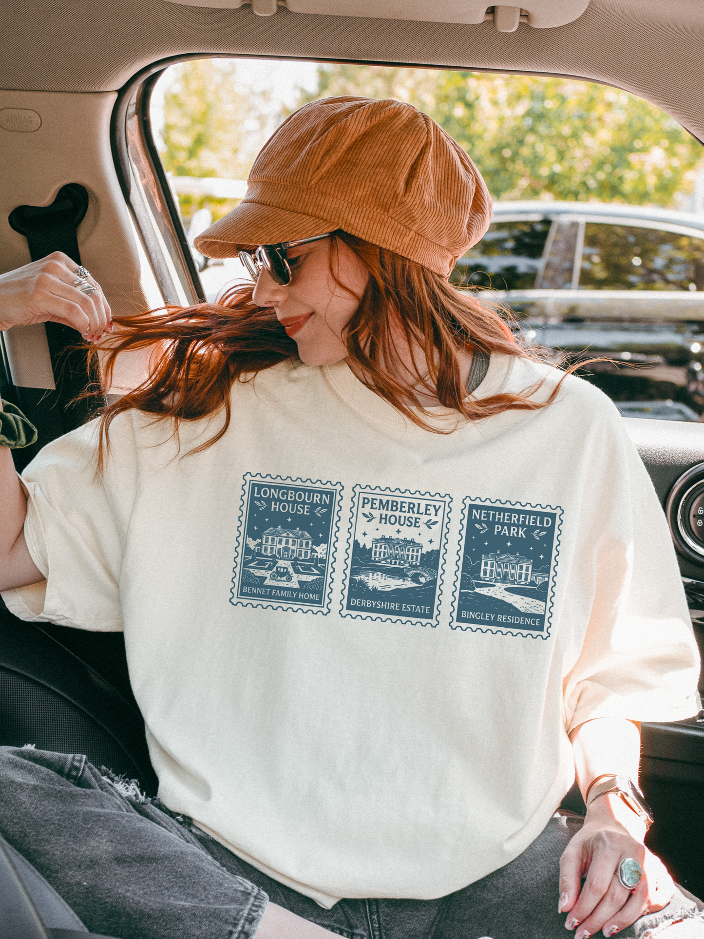 woman sitting in car wearing cream t shirt with Pride and Prejudice stamp illustration featuring Longbourn House Pemberley House and Netherfield Park casual outfit