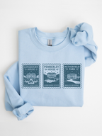 folded light blue sweatshirt with vintage stamp style design featuring Longbourn House Pemberley House and Netherfield Park inspired by Jane Austen