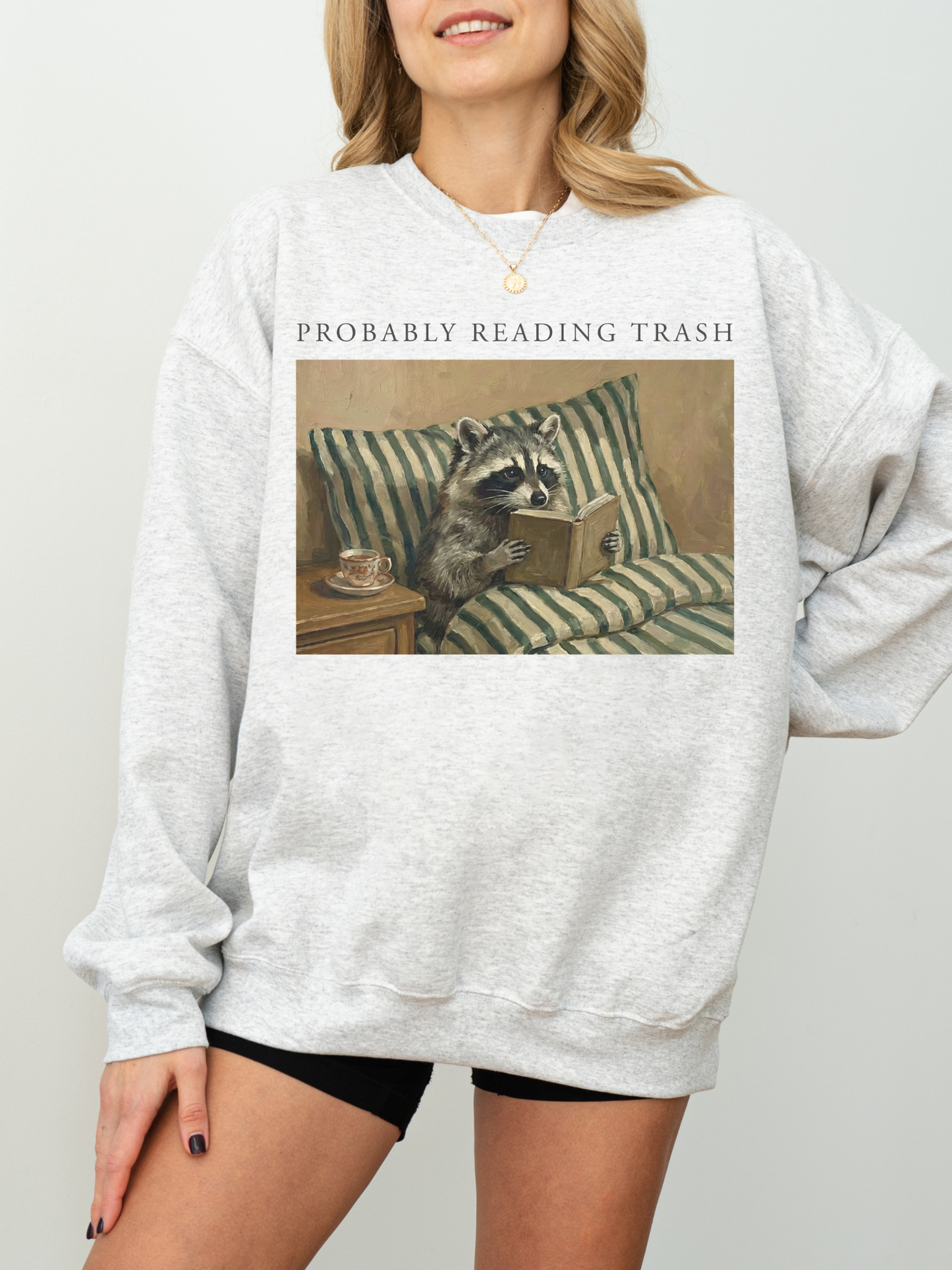 woman wearing oversized grey sweatshirt featuring probably reading trash raccoon reading book illustration relaxed fit cozy bookish outfit